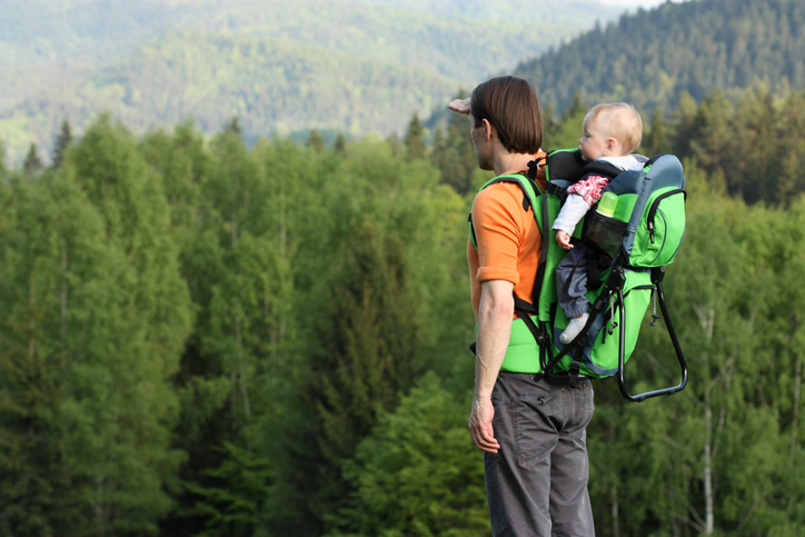 Young father is hiking with 1 year old son in backpack baby carrier